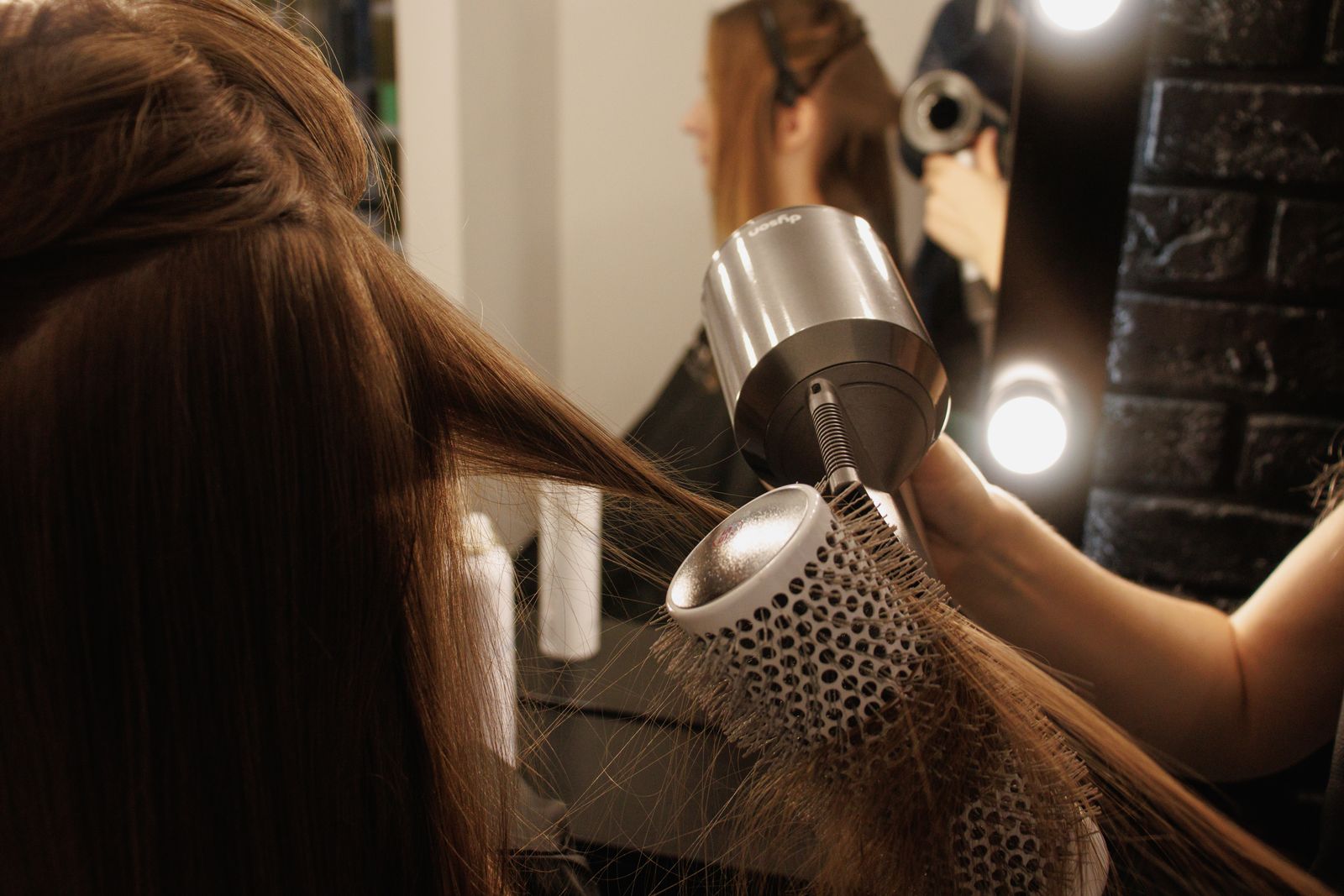 A stylist blow drying a client's long hair with a round brush